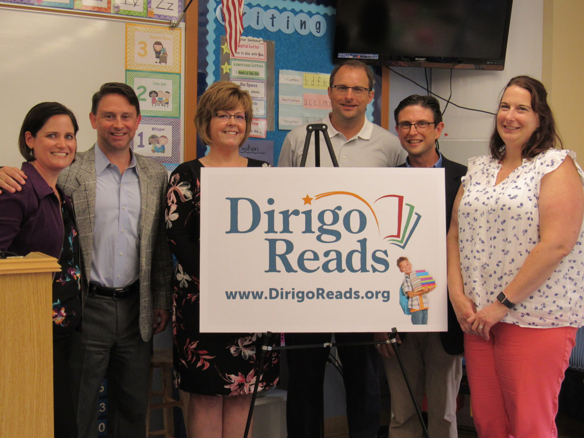 photo of dan and karen cashman with partners behind a dirigo reads poster